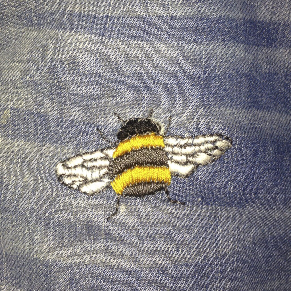 Broek na herstel met een hommel borduursel over de vlek, uitgevoerd door Curieus Retouches Begijnendijk.